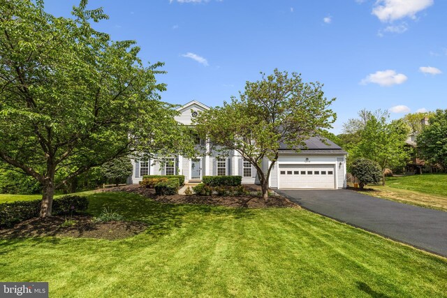 obstructed view of property featuring an attached garage, a front lawn, roof mounted solar panels, and driveway