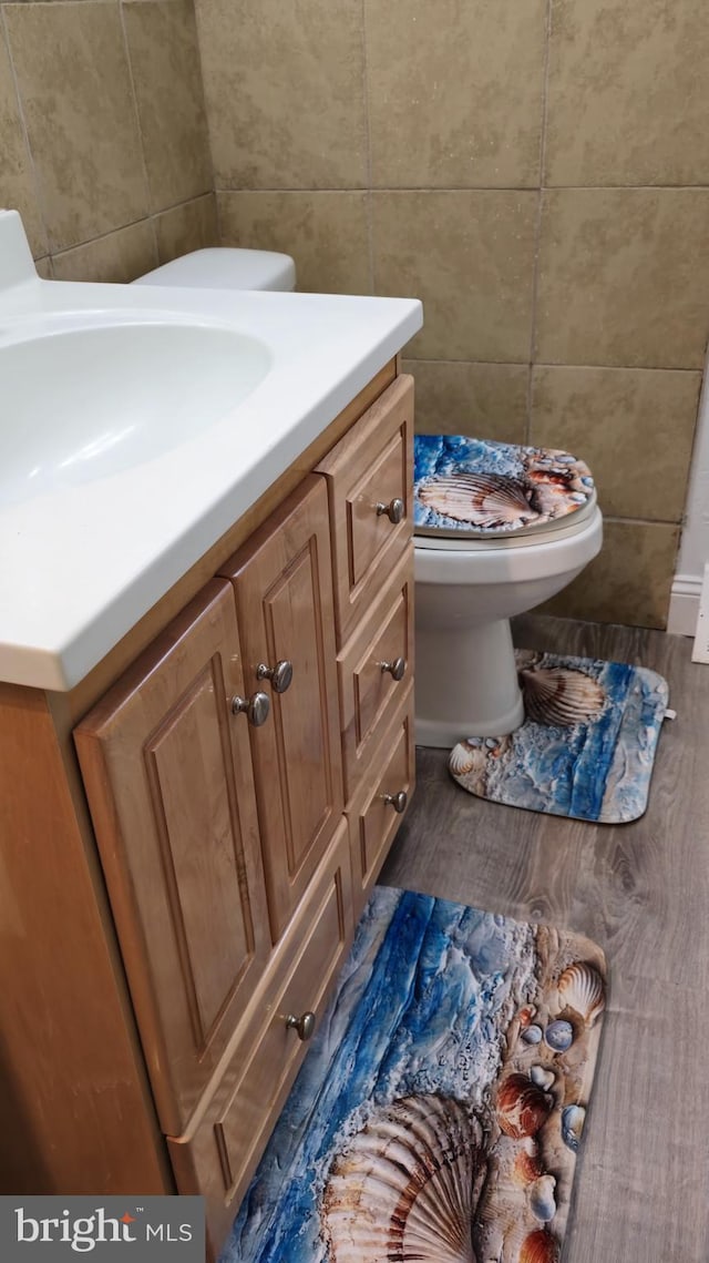 bathroom with tile walls, toilet, vanity, and wood finished floors