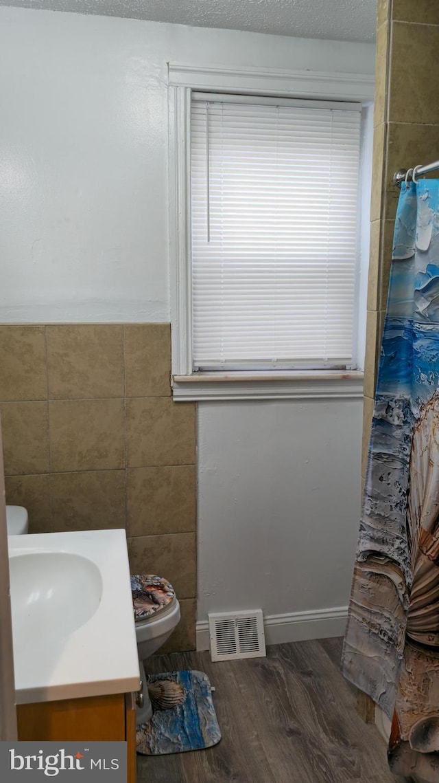 full bathroom featuring toilet, tile walls, visible vents, wood finished floors, and vanity