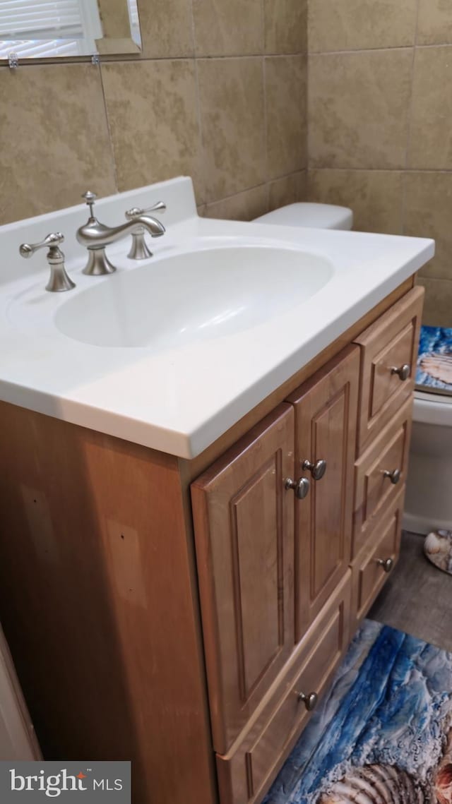 bathroom with tile walls, wood finished floors, vanity, and toilet