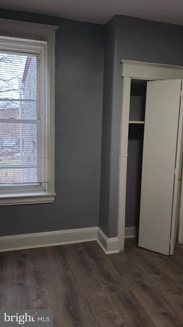 unfurnished bedroom featuring wood finished floors, a closet, and baseboards
