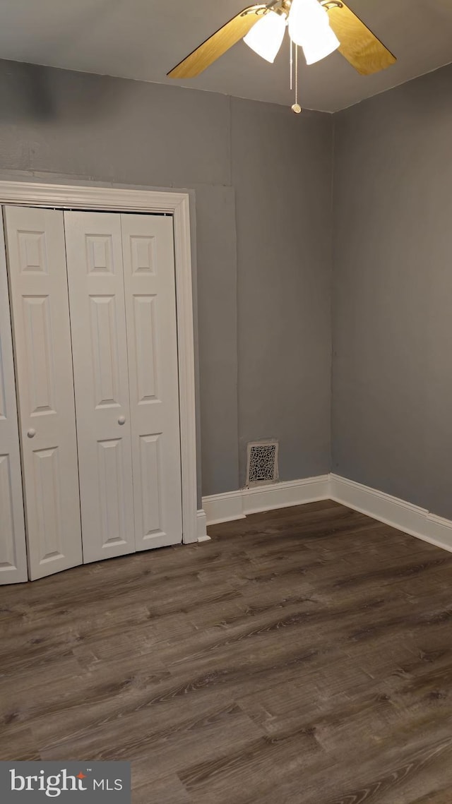unfurnished bedroom featuring a closet, dark wood-type flooring, a ceiling fan, visible vents, and baseboards