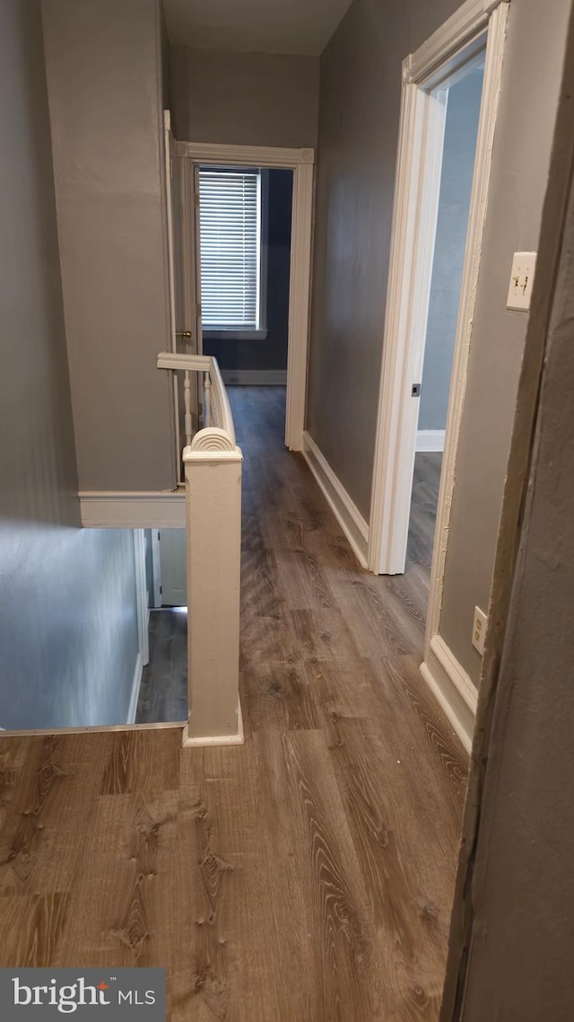 hallway with baseboards, wood finished floors, and an upstairs landing