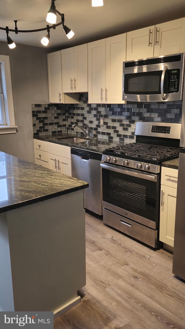 kitchen featuring light wood-style flooring, a sink, white cabinetry, backsplash, and appliances with stainless steel finishes