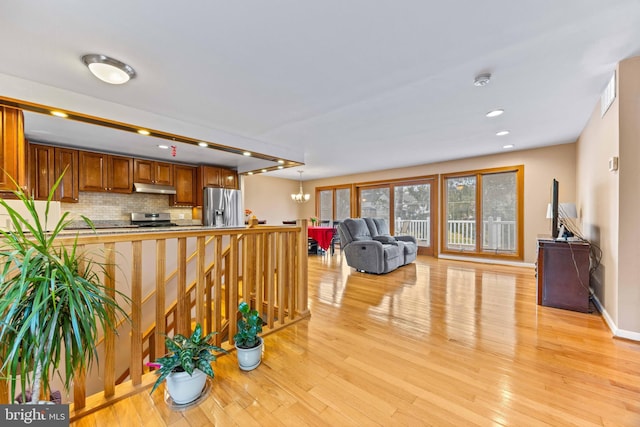 interior space with stainless steel appliances, under cabinet range hood, open floor plan, and light wood-style floors
