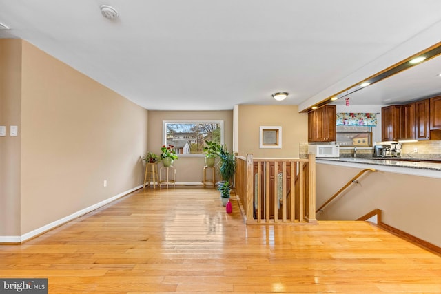 kitchen featuring a sink, light wood-type flooring, baseboards, white microwave, and brown cabinetry