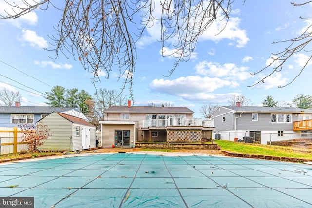 rear view of property with a shed, a deck, fence, an outbuilding, and a fenced in pool