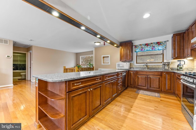 kitchen featuring light wood finished floors, stainless steel appliances, a sink, backsplash, and open shelves