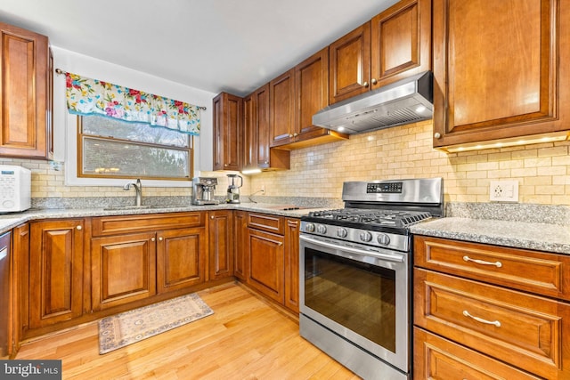 kitchen featuring light stone counters, a sink, decorative backsplash, appliances with stainless steel finishes, and under cabinet range hood