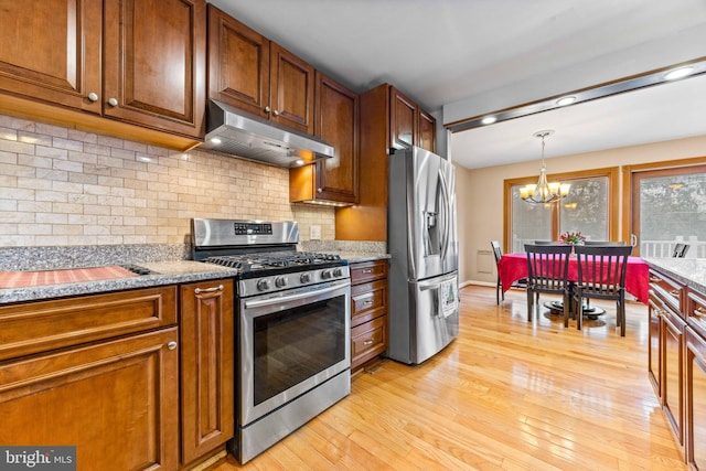 kitchen featuring light wood-type flooring, an inviting chandelier, backsplash, under cabinet range hood, and appliances with stainless steel finishes