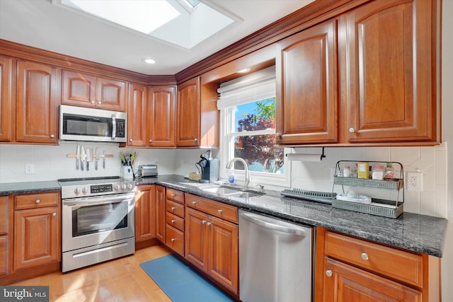 kitchen featuring brown cabinets, appliances with stainless steel finishes, a sink, and dark stone countertops