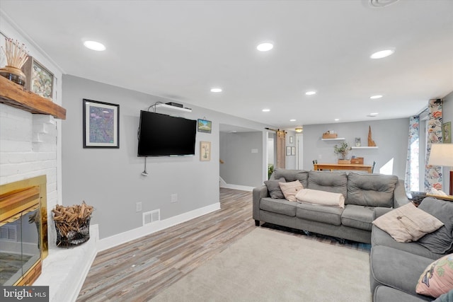 living area with visible vents, a brick fireplace, baseboards, recessed lighting, and light wood-type flooring
