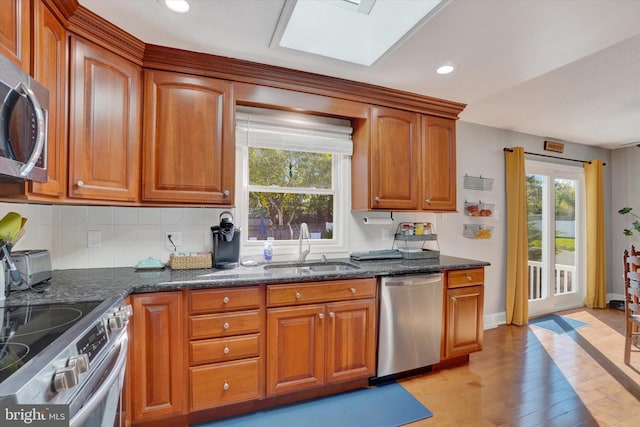 kitchen featuring brown cabinets, a sink, dark stone countertops, stainless steel appliances, and light wood-type flooring