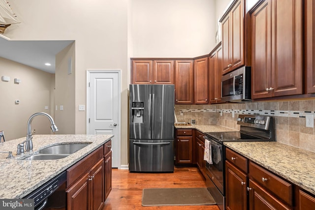 kitchen featuring a sink, stainless steel appliances, decorative backsplash, light stone counters, and wood finished floors