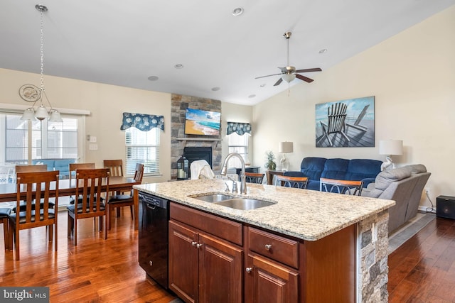 kitchen with black dishwasher, a stone fireplace, a sink, dark wood-style floors, and open floor plan