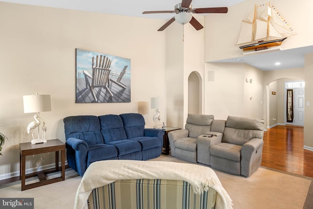 living room featuring arched walkways, wood finished floors, ceiling fan, baseboards, and a high ceiling