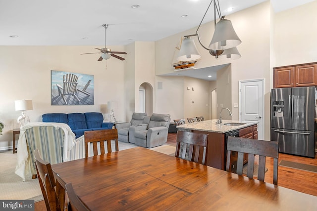 dining space featuring light wood-type flooring, a ceiling fan, high vaulted ceiling, and arched walkways