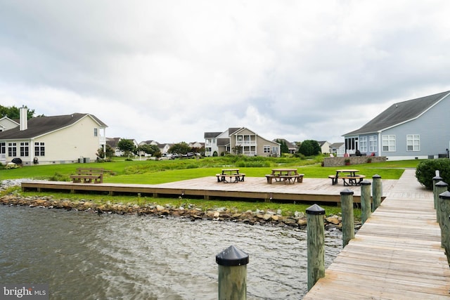 view of dock with a lawn, a water view, and a residential view