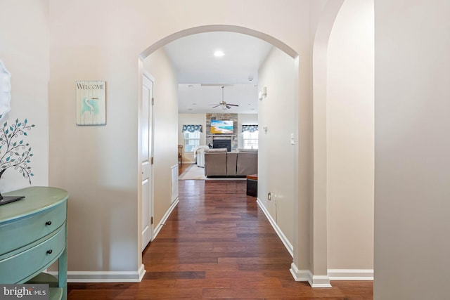 hallway with arched walkways, wood finished floors, and baseboards