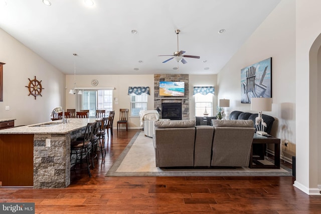 living room featuring lofted ceiling, ceiling fan, a fireplace, and dark wood finished floors