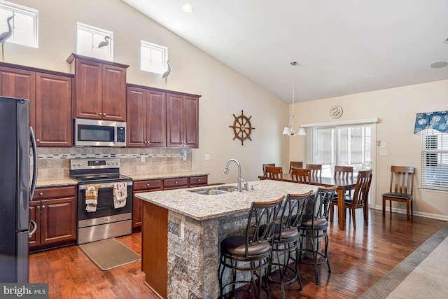kitchen with a sink, appliances with stainless steel finishes, a breakfast bar, dark wood finished floors, and backsplash