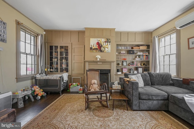 living area with a wall mounted AC, wood finished floors, a wealth of natural light, and a fireplace