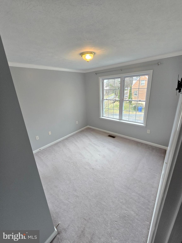 carpeted empty room with baseboards, visible vents, and crown molding