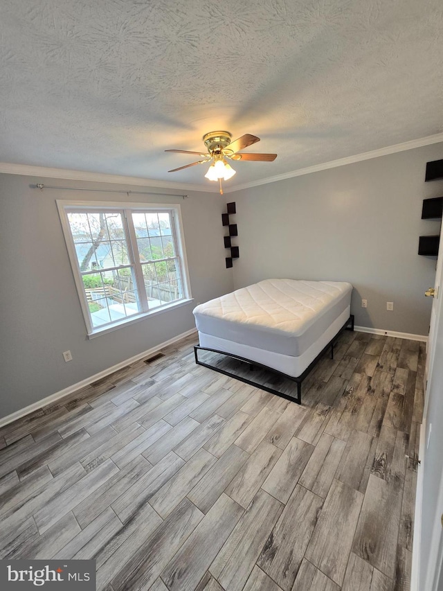 bedroom with a textured ceiling, wood finished floors, ornamental molding, and baseboards