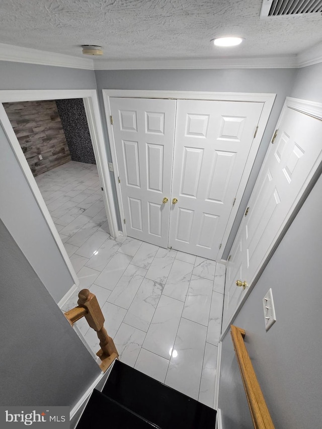 entrance foyer with a textured ceiling, visible vents, crown molding, and marble finish floor