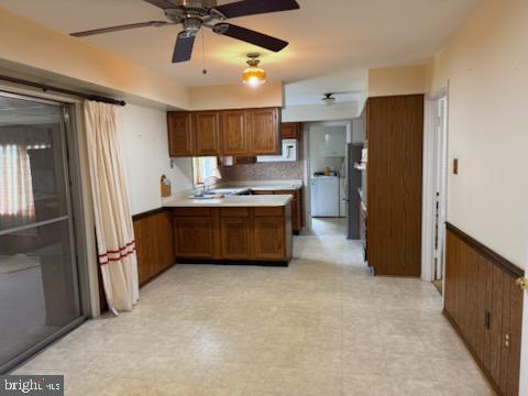 kitchen featuring brown cabinetry, a wainscoted wall, washer / dryer, light floors, and light countertops