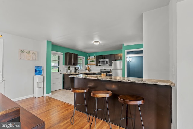 6842 Queens Ferry Rd, Baltimore, MD 21239 - kitchen with appliances with stainless steel finishes, a peninsula, decorative backsplash, light wood-style floors, and light stone counters