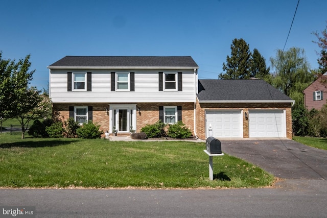 colonial house featuring brick siding, a garage, a front lawn, and driveway