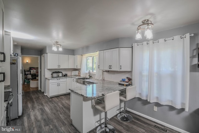 kitchen with dark wood-style flooring, light stone countertops, freestanding refrigerator, a peninsula, and white cabinetry