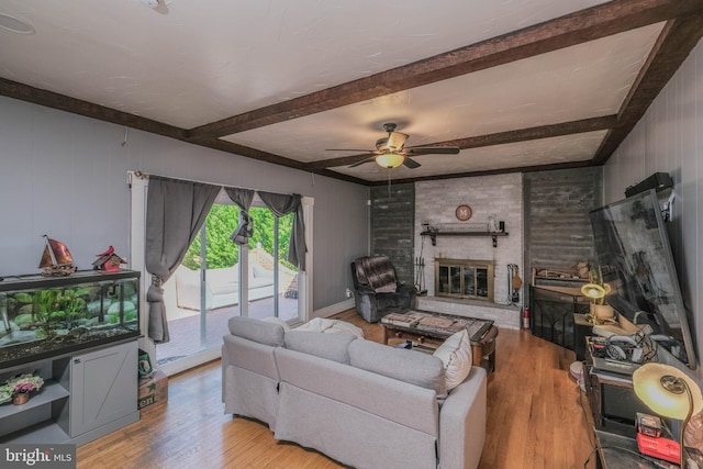 living room with beamed ceiling, a ceiling fan, wood finished floors, and a brick fireplace