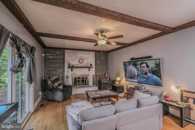 living area with wood-type flooring, a ceiling fan, beamed ceiling, and a fireplace