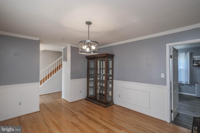 unfurnished dining area with wainscoting, a chandelier, wood finished floors, visible vents, and stairway