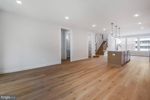 kitchen with baseboards, a center island with sink, light wood-style flooring, and a sink