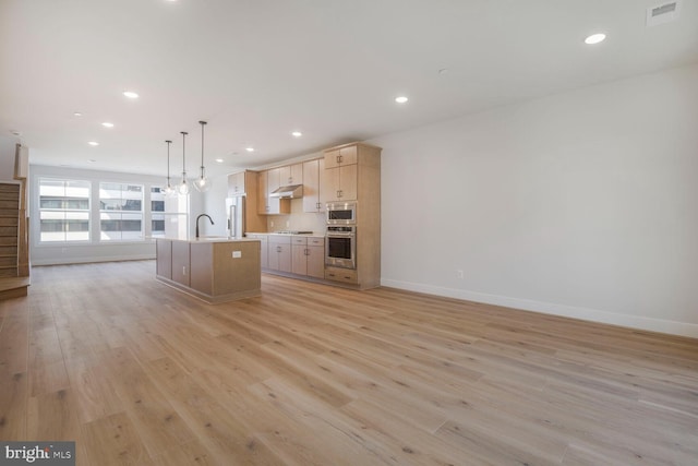 kitchen with a sink, freestanding refrigerator, baseboards, under cabinet range hood, and a center island with sink
