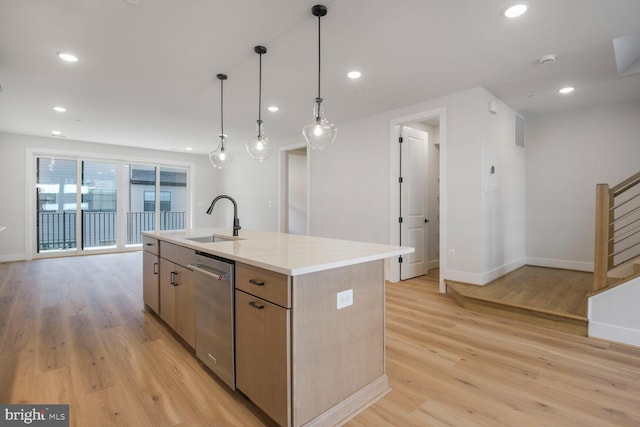 kitchen with stainless steel dishwasher, light wood-style flooring, a sink, light countertops, and a kitchen island with sink