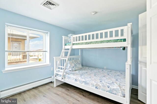 bedroom with wood finished floors, visible vents, and a baseboard heating unit