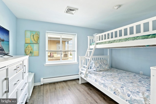 bedroom featuring baseboards, visible vents, wood finished floors, and a baseboard heating unit