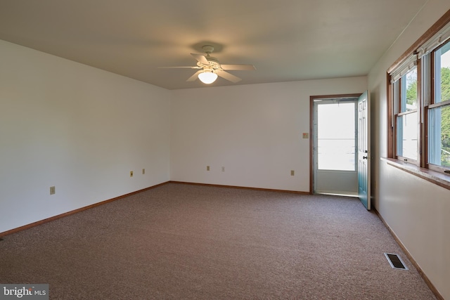 empty room with light colored carpet, a ceiling fan, baseboards, and visible vents