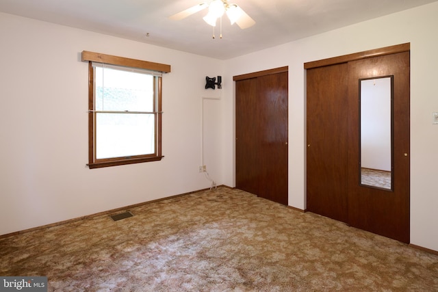unfurnished bedroom featuring two closets, ceiling fan, visible vents, and carpet