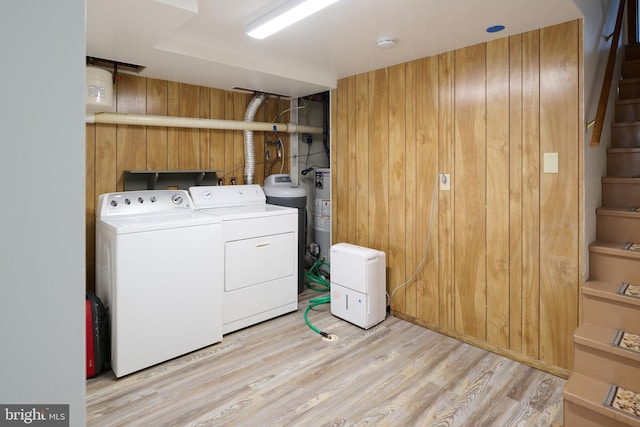 washroom with light wood-type flooring, wood walls, independent washer and dryer, and laundry area