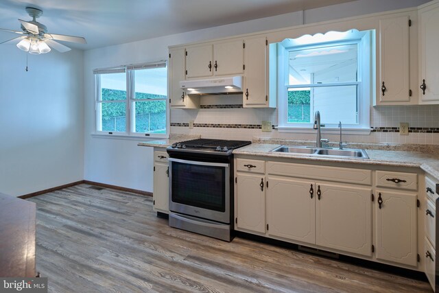 kitchen with a ceiling fan, backsplash, stainless steel gas stove, a sink, and under cabinet range hood