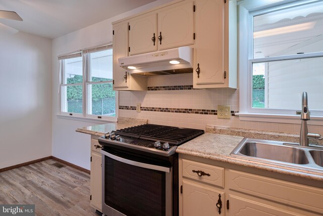 kitchen featuring a sink, stainless steel range with gas cooktop, baseboards, tasteful backsplash, and under cabinet range hood