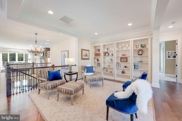 sitting room with wood finished floors, an upstairs landing, visible vents, a chandelier, and ornamental molding