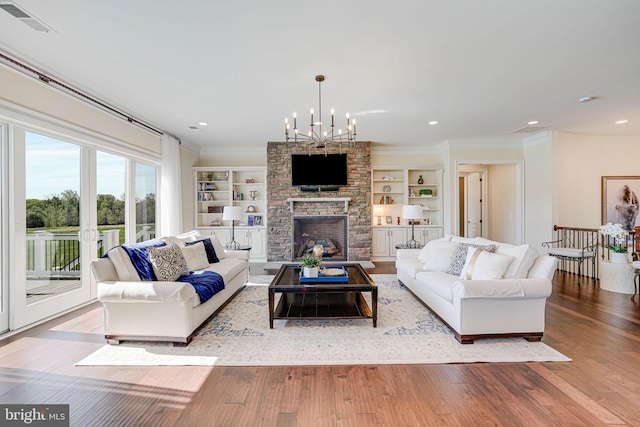 living area with a notable chandelier, visible vents, crown molding, wood finished floors, and a fireplace