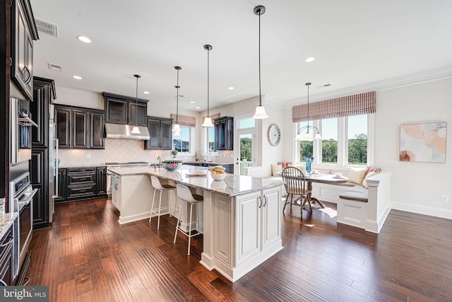 kitchen with backsplash, dark wood-style floors, a breakfast bar area, and under cabinet range hood