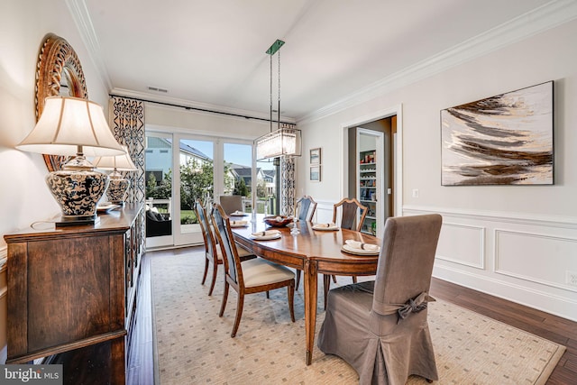 dining area with crown molding, visible vents, wood finished floors, and wainscoting